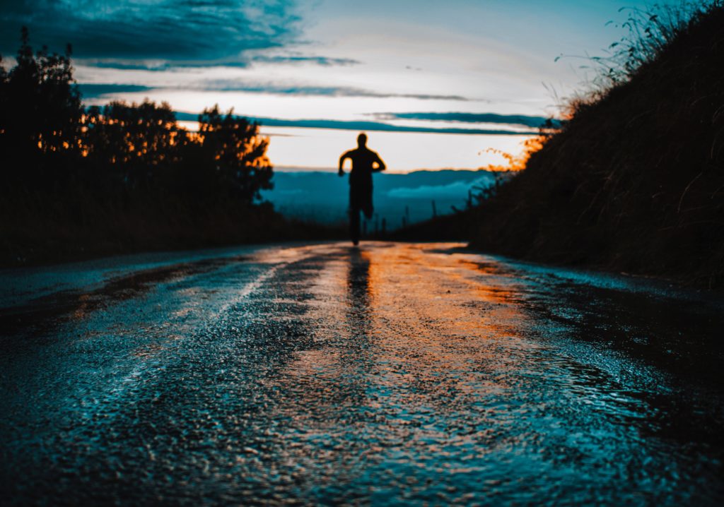 a figure running toward the horizon on a damp street