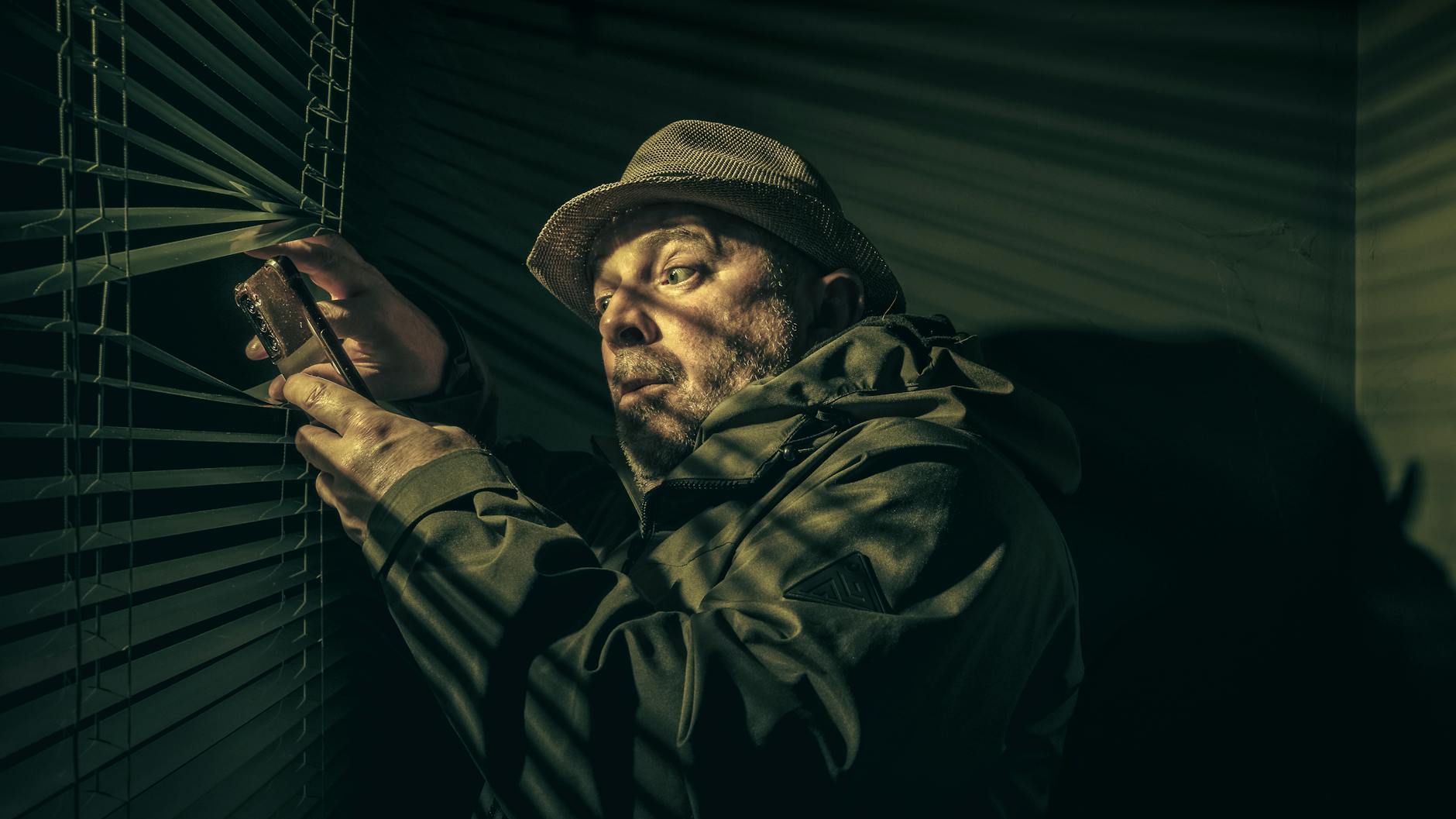 suspicious man peering through blinds at night